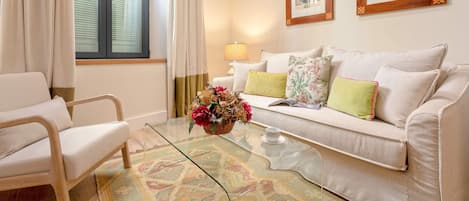 A well-lit living room with a sofa, armchair, and a glass coffee table with a floral centerpiece.