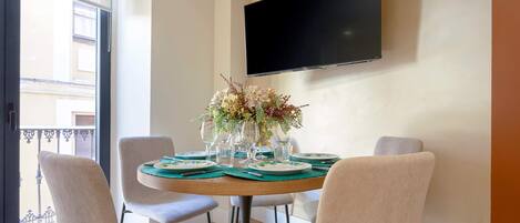 Un coin repas avec une table ronde dressée pour quatre personnes, entourée de quatre chaises. Un téléviseur à écran plat est fixé au mur, au-dessus de la table.