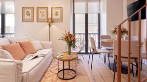 A living room with a sofa, coffee table, and chairs, a balcony with a railing, and a TV mounted on the wall. - Genteel Home Rodrigo Caro (Seville)