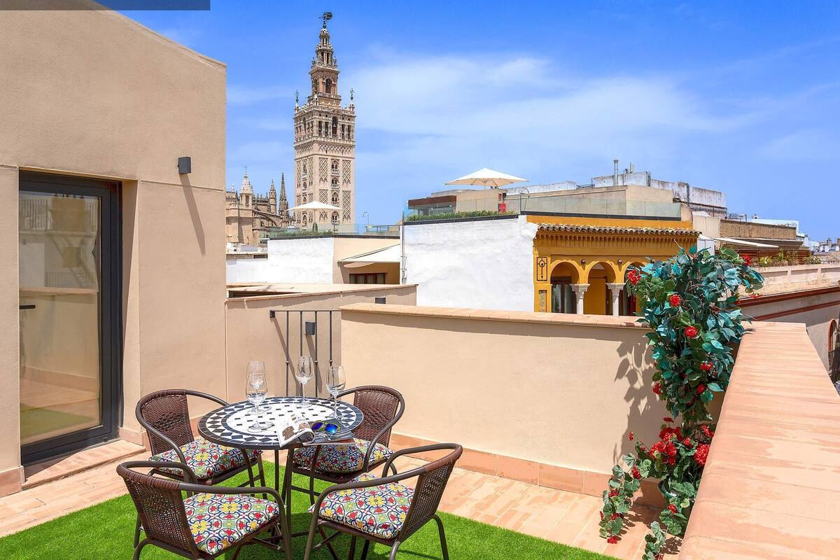 A rooftop terrace with a table and chairs, a view of a historic tower, and a building with arches.