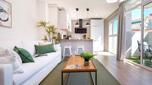Ein modernes Wohnzimmer mit einer Couch, einem Couchtisch und einer Küchenzeile im Hintergrund.