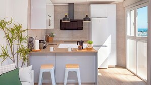 Eine moderne Küche mit einer zentralen Kochinsel, zwei Barhocker, einer Pendelleuchte und Meerblick durch große Fenster.