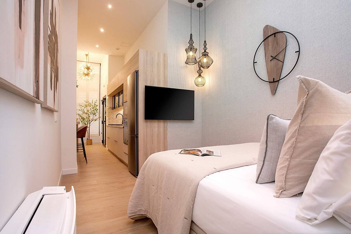A modern bedroom with a bed, a mounted TV, and pendant lighting.