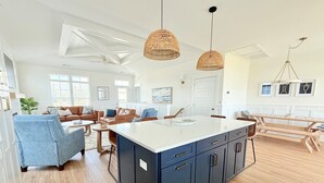 Un vaste espace de vie comprenant un grand îlot central, une table à manger et une cuisine avec des meubles en bois et un plan de travail blanc.