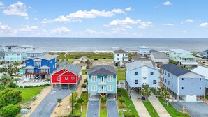 Une zone résidentielle côtière avec des maisons sur pilotis, un ciel dégagé et l’océan en toile de fond.