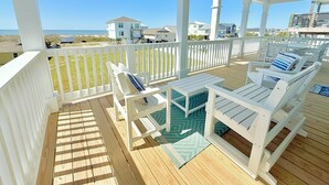 Une terrasse couverte avec des meubles blancs, une piscine et une vue sur les maisons et l’océan.