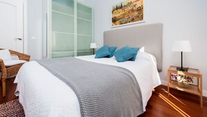 A modern bedroom with a large bed, a wicker chair, a glass partition, and a painting on the wall. - Genteel Home Plaza Nueva (Seville)