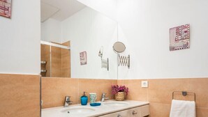 A modern bathroom with a large mirror, two sinks, a wooden shelf with towels, and decorative wall art. - Genteel Home Plaza Nueva (Seville)