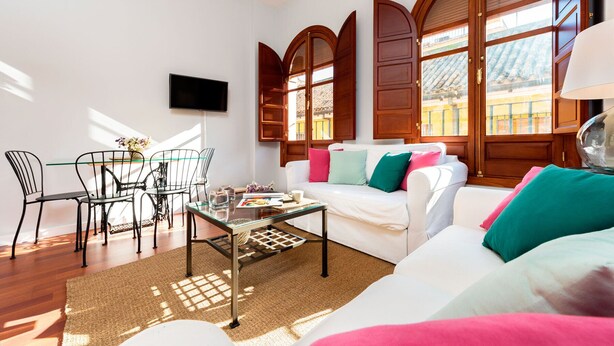 A modern living room with a white sofa, colorful cushions, a glass coffee table, and a TV mounted on the wall. - Genteel Home Plaza Nueva (Seville)