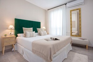 Un dormitorio ordenado con una cama grande, mesitas de noche, un banco y un espejo.