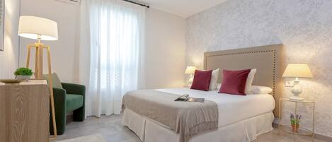 Un dormitorio ordenado con una cama grande, lámparas de noche, un sillón verde y una mesita con una planta.
