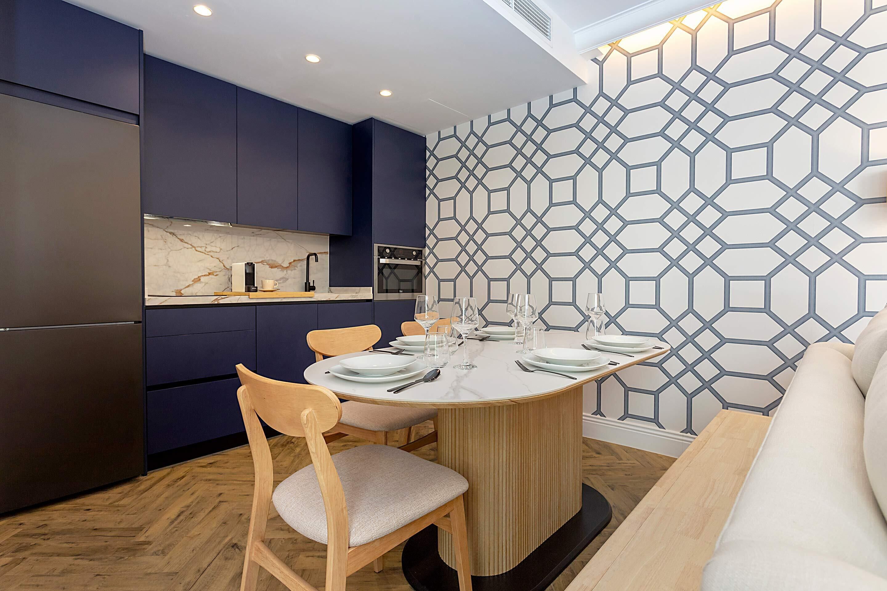 A modern kitchen with dark cabinets, a marble countertop, and a dining area with a round table set for four.