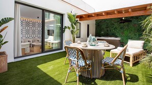 Een modern terras buiten met een ronde tafel, rieten stoelen en een serre.