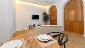 Een eetgedeelte met een houten tafel gedekt voor twee personen, een bank en een aan de muur bevestigde televisie.