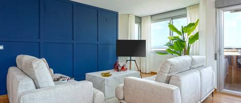 Un salon avec un mur d’accent bleu, une table basse en marbre, un canapé gris, un téléviseur à écran plat posé sur un meuble et une grande plante.