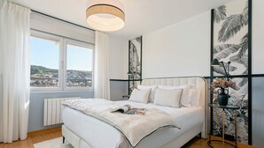Ένα υπνοδωμάτιο με ένα μεγάλο κρεβάτι, ένα κομοδίνο με ένα φωτιστικό, θέα προς το εξωτερικό και ένα καλοριφέρ.