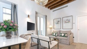 A modern living room with a dining table, chairs, a sofa, and a coffee table. There are two framed artworks on the wall, a flat-screen TV mounted above the sofa, and a potted plant on the table. - Genteel Home Teodosio (Seville)