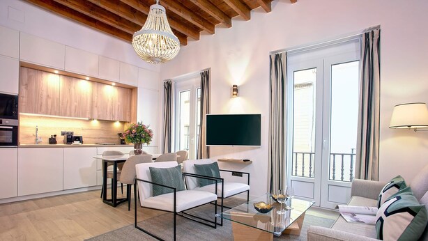 A modern living room with a sofa, a coffee table, and a TV. There is a kitchen area with cabinets and a dining table. - Genteel Home Teodosio (Seville)