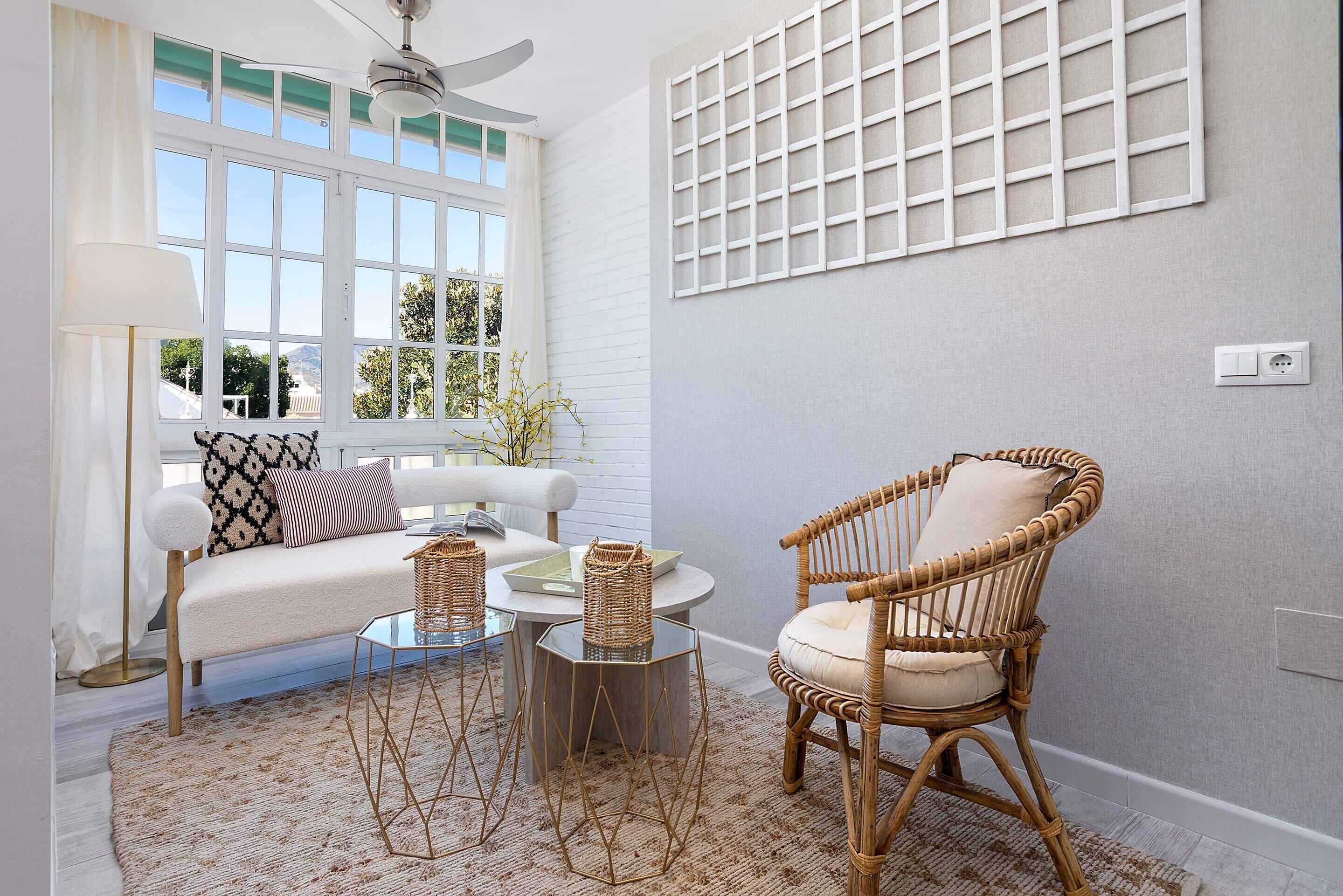 A room with a white sofa, a wicker chair, a glass coffee table, and a patterned rug.