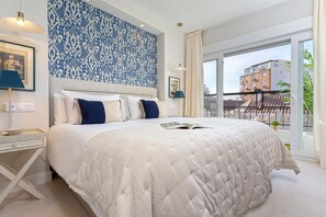 A modern bedroom with a large bed, a patterned wall, and a view of buildings through a large window. - Genteel Home Plaza del Teatro (Málaga)