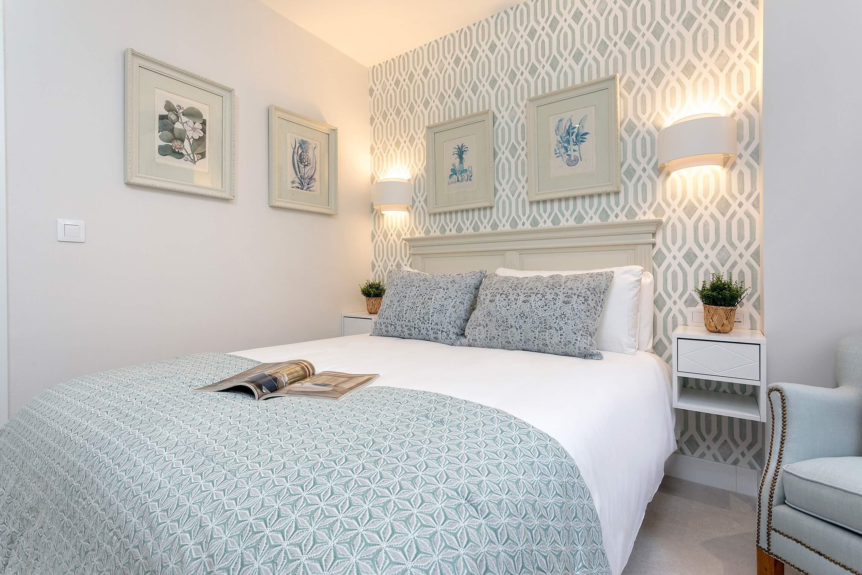 Een netjes ingerichte slaapkamer met een bedovertrek met dessin, ingelijste kunst aan de muur en bedlampjes.