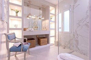 A bathroom with a marble shower, a white vanity with a mirror, and a wicker chair. - Genteel Home Plaza del Teatro (Málaga)