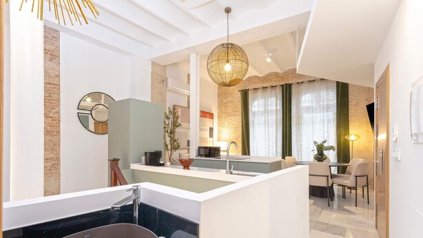 A modern bathroom with a large bathtub, a sink, and a mirror. There is a dining area with a table and chairs visible through an open doorway. - Genteel Home Gran Poder (Seville)