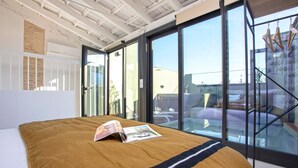 A modern bedroom with a large bed, a magazine on the bed, and a view of the outside through large windows. - Genteel Home Gran Poder (Seville)