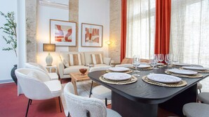A dining area with a dark table set for six, surrounded by white chairs, with artwork on the walls and a red curtain to the right. - Genteel Home Gran Poder (Seville)