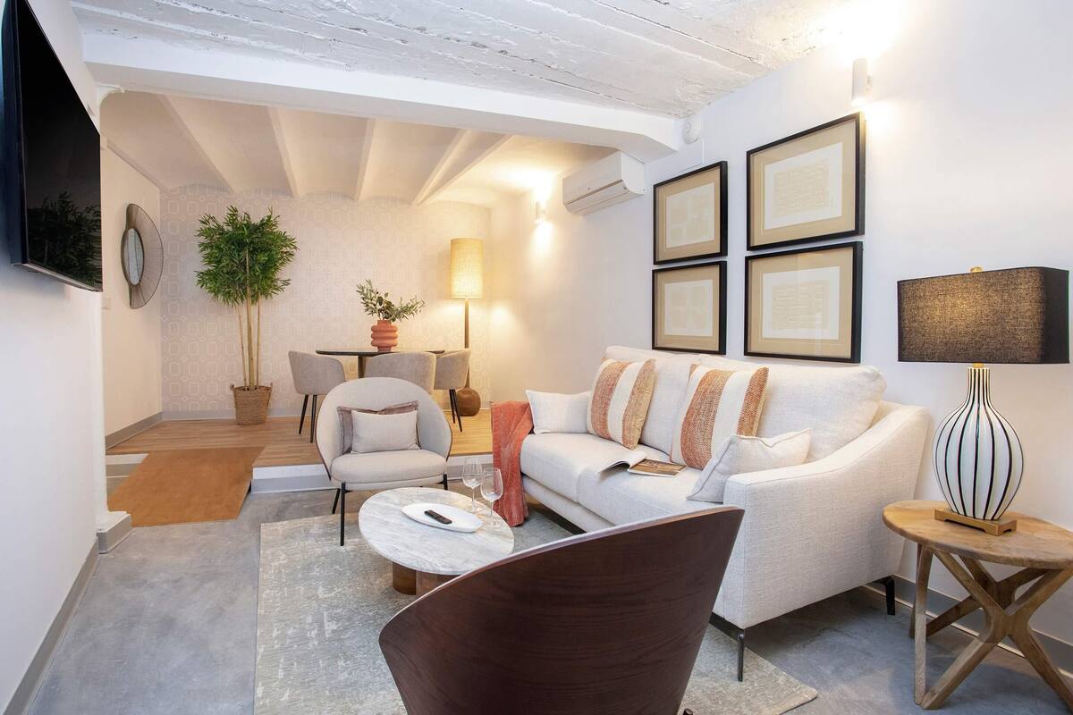 Un salon moderne avec un canapé blanc, un fauteuil marron et une table basse. On peut y voir des tableaux encadrés au mur, une lampe et une plante en pot.