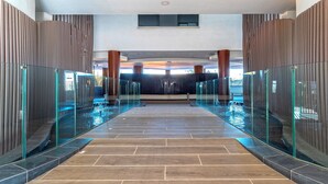 A modern indoor pool area with glass railings and a tiled floor. - Genteel Home Infinity (Estepona)