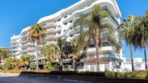 A modern multi-story hotel with balconies, palm trees, and a clear blue sky. - Genteel Home Infinity (Estepona)