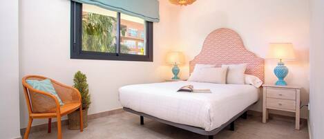 A bedroom with a bed, two bedside tables, a chair, a window with a view, and a hanging light fixture.