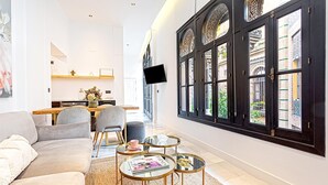 A modern living room with a sofa, coffee table, and chairs, a dining area with a table and chairs, and large windows with decorative ironwork. - Genteel Home Placentines (Seville)