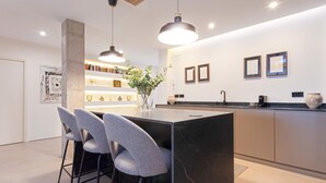 A modern kitchen with a marble island, bar stools, pendant lighting, and a bookshelf with decorative items. - Genteel Home Pureza (Seville)