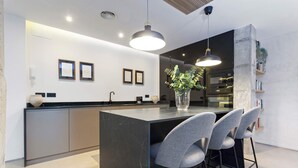 A modern kitchen with a central island, bar stools, pendant lighting, and a built-in oven. - Genteel Home Pureza (Seville)