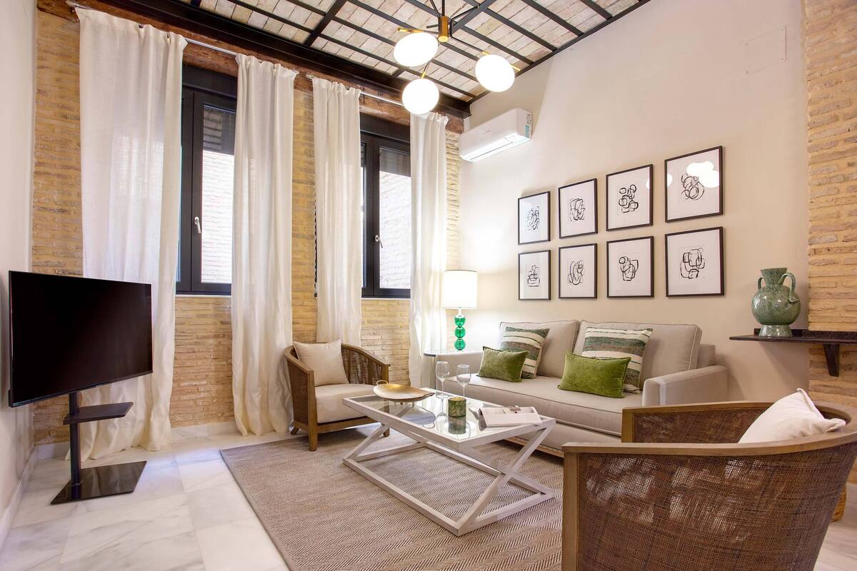A modern living room with a flat-screen TV, wicker furniture, a glass coffee table, and a brick wall.