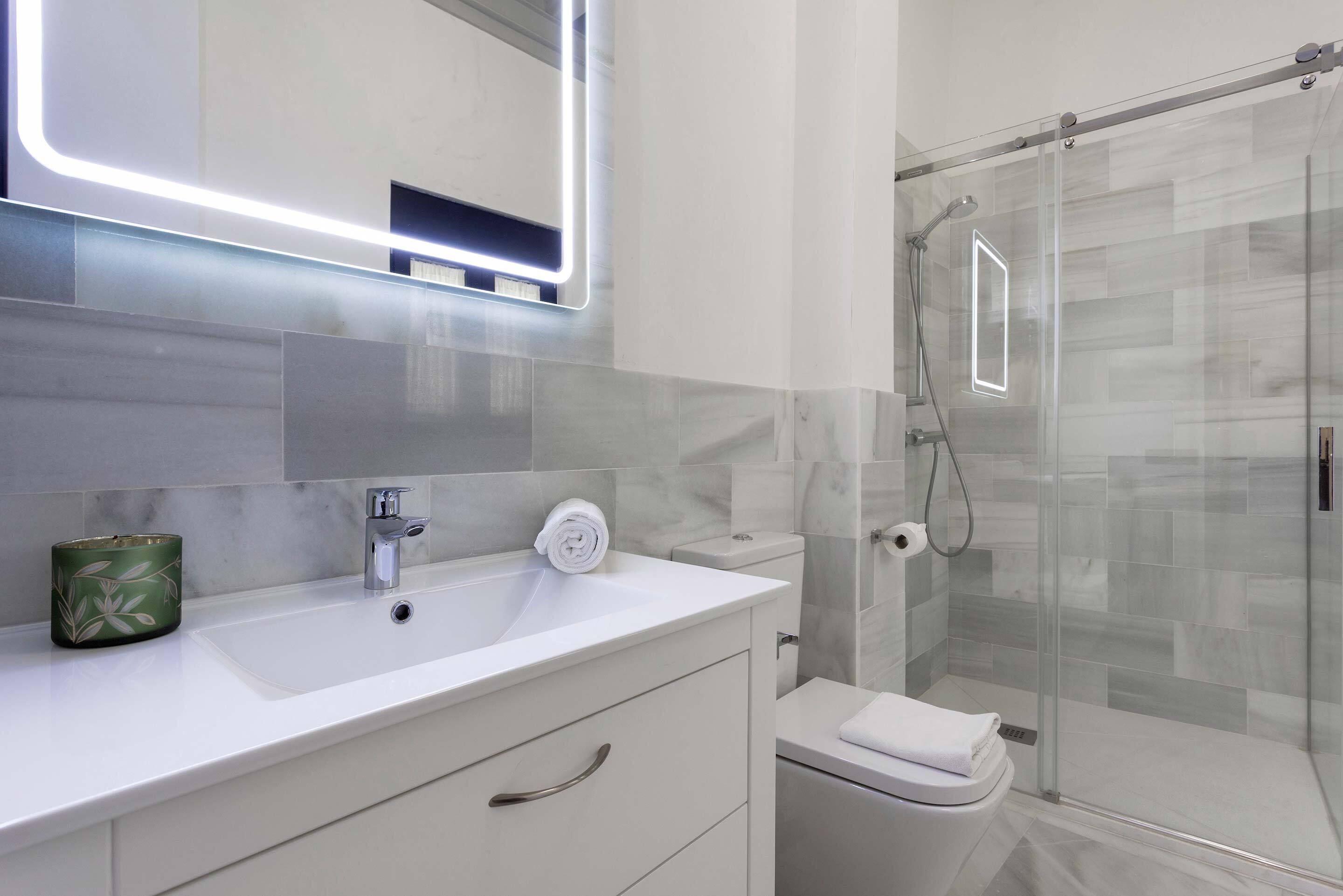 A modern bathroom with a white sink, a glass shower enclosure, and a toilet.