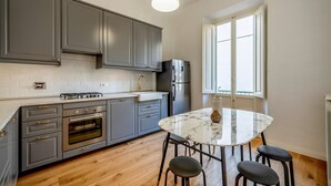 A modern kitchen with grey cabinets, a built-in oven, and a marble dining table with four chairs. - Genteel Home Vittorio Emanuele (Florence)