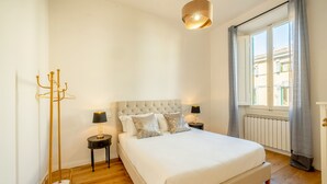 A bedroom with a large bed, two bedside tables with lamps, a floor lamp, and a window with curtains. - Genteel Home Vittorio Emanuele (Florence)