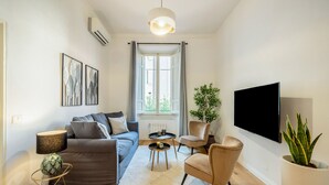 Een moderne woonkamer met een bank, fauteuils, een salontafel, een televisie en een potplant.
