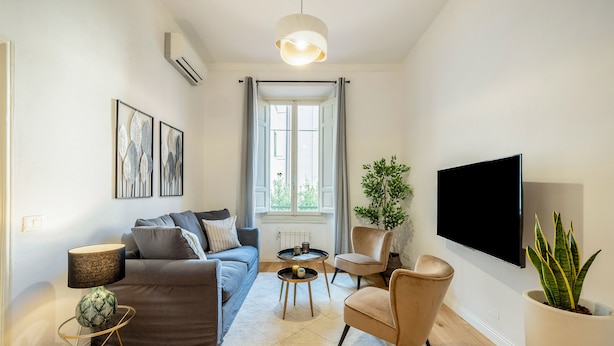 A modern living room with a sofa, armchairs, a coffee table, a TV, and a potted plant. - Genteel Home Vittorio Emanuele (Florence)