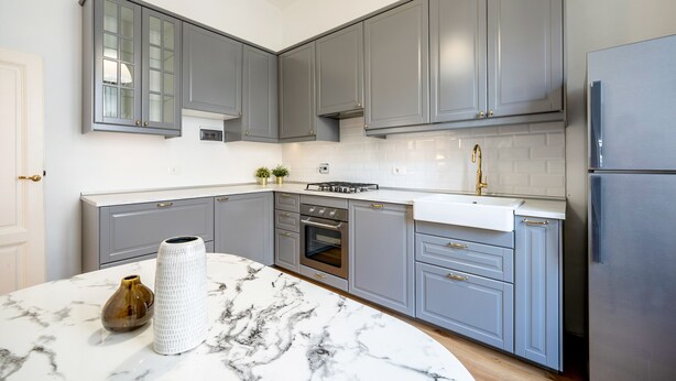 Een moderne keuken met grijze kastjes, een wit aanrecht en een marmeren eiland.
