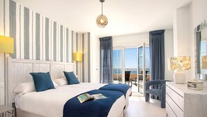 Une chambre d’hôtel avec un grand lit, un bureau, une chaise et une vue sur la mer.