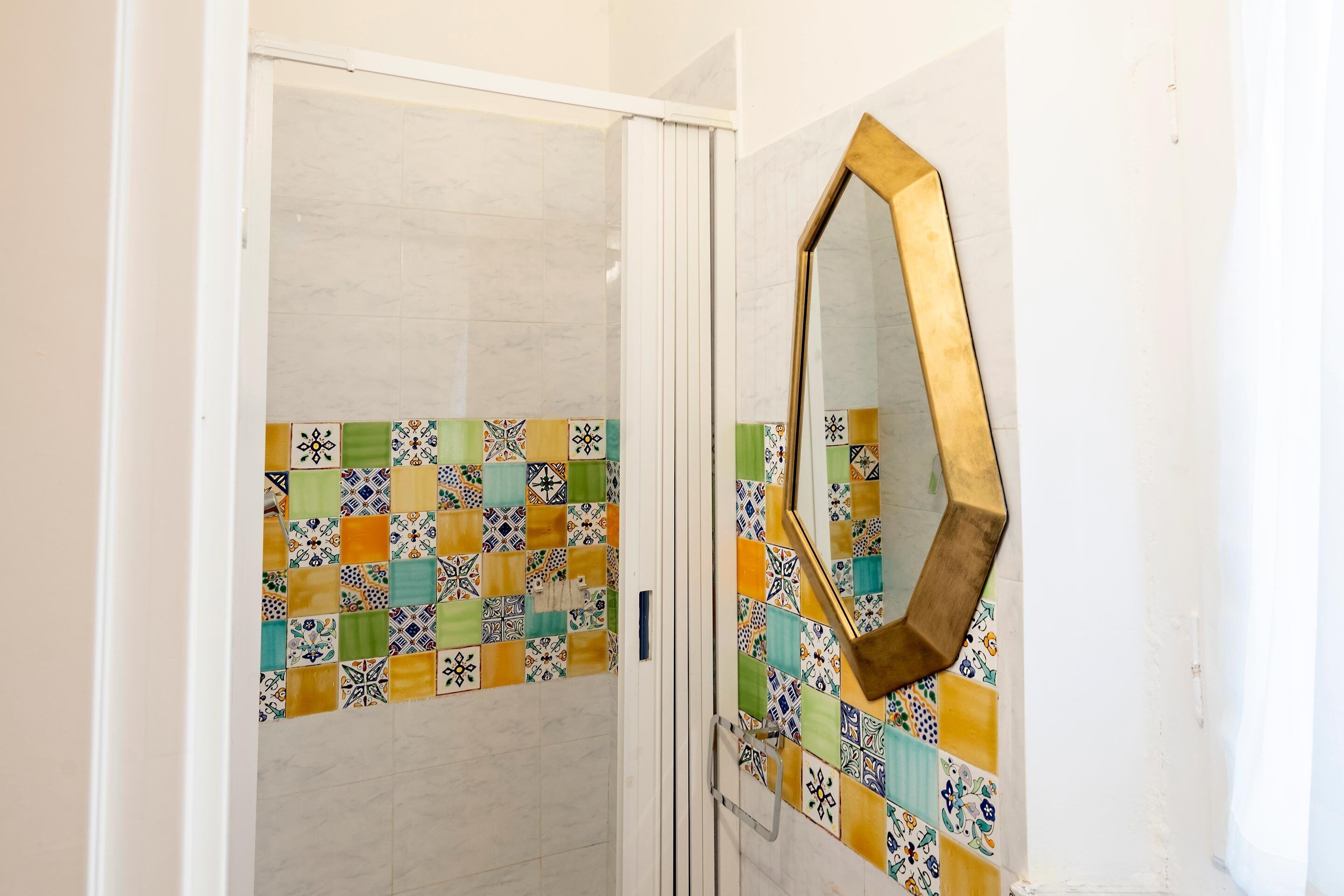 A bathroom with a tiled wall, a mirror, and a door.