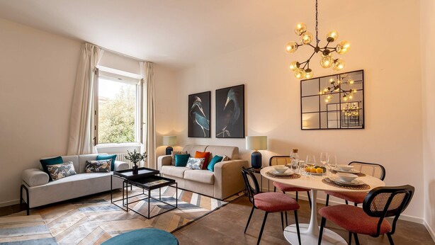 Una sala de estar moderna con sofá, mesa de comedor y sillas, una araña y obras de arte en las paredes.