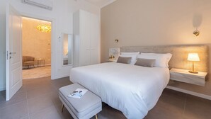 A modern bedroom with a large bed, a bedside table with a lamp, a small bedside table with a plant, and a mirror above the bed. - Genteel Home Cittadella (Florence)