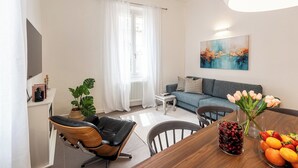 A modern living room with a sofa, a dining table with fruit, a chair, a plant, and a painting on the wall. - Genteel Home Cittadella (Florence)