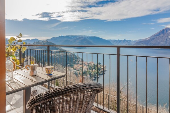A balcony with a view of a lake and mountains, a wicker chair, a table with a cup and a pitcher, and a railing. - Panorama del Lago in Perledo (Perledo)