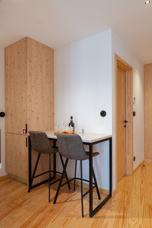 Eine kleine Küche mit einem Holzkorpus, einer weißen Arbeitsplatte, zwei grauen Stühlen und einem Tisch mit Speisen und Getränken.
